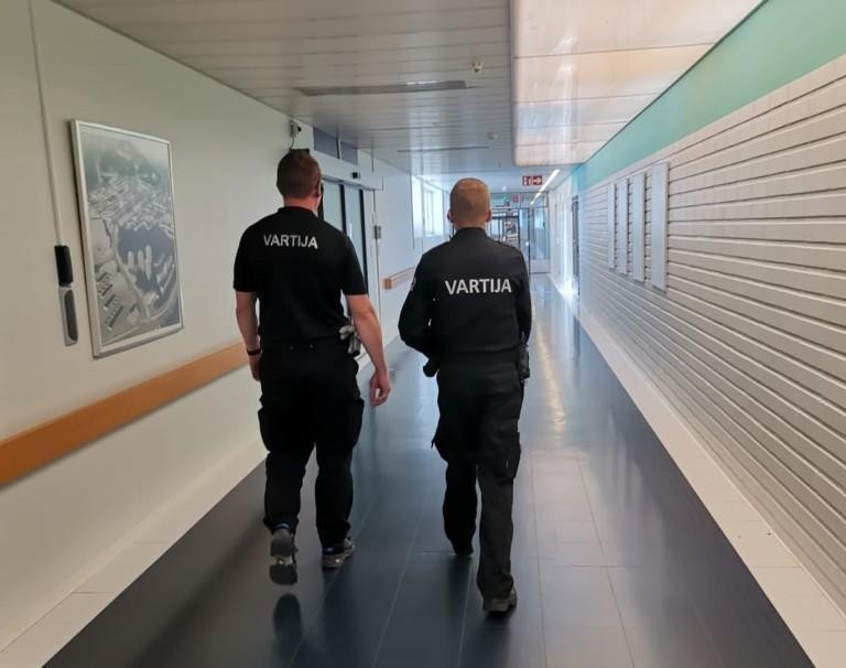  Kaksi vartijaa kävelee sairaalan käytävällä.